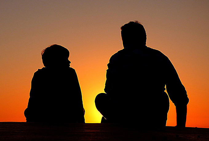 father and son sat together watching a sunset