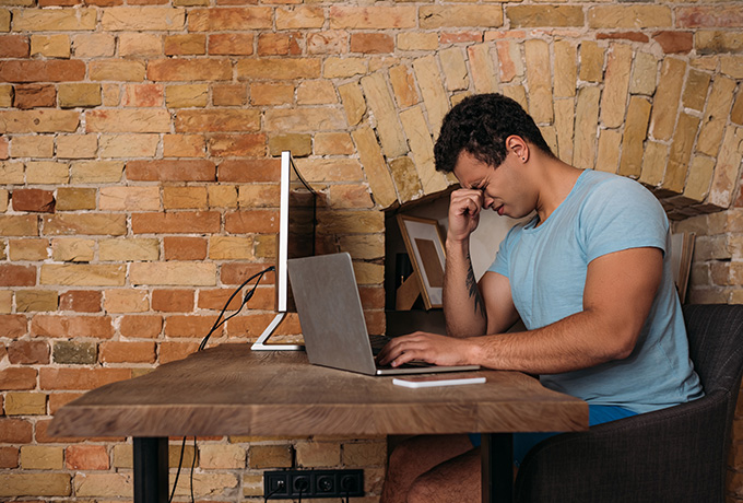 depressed man sat at a table looking at a laptop