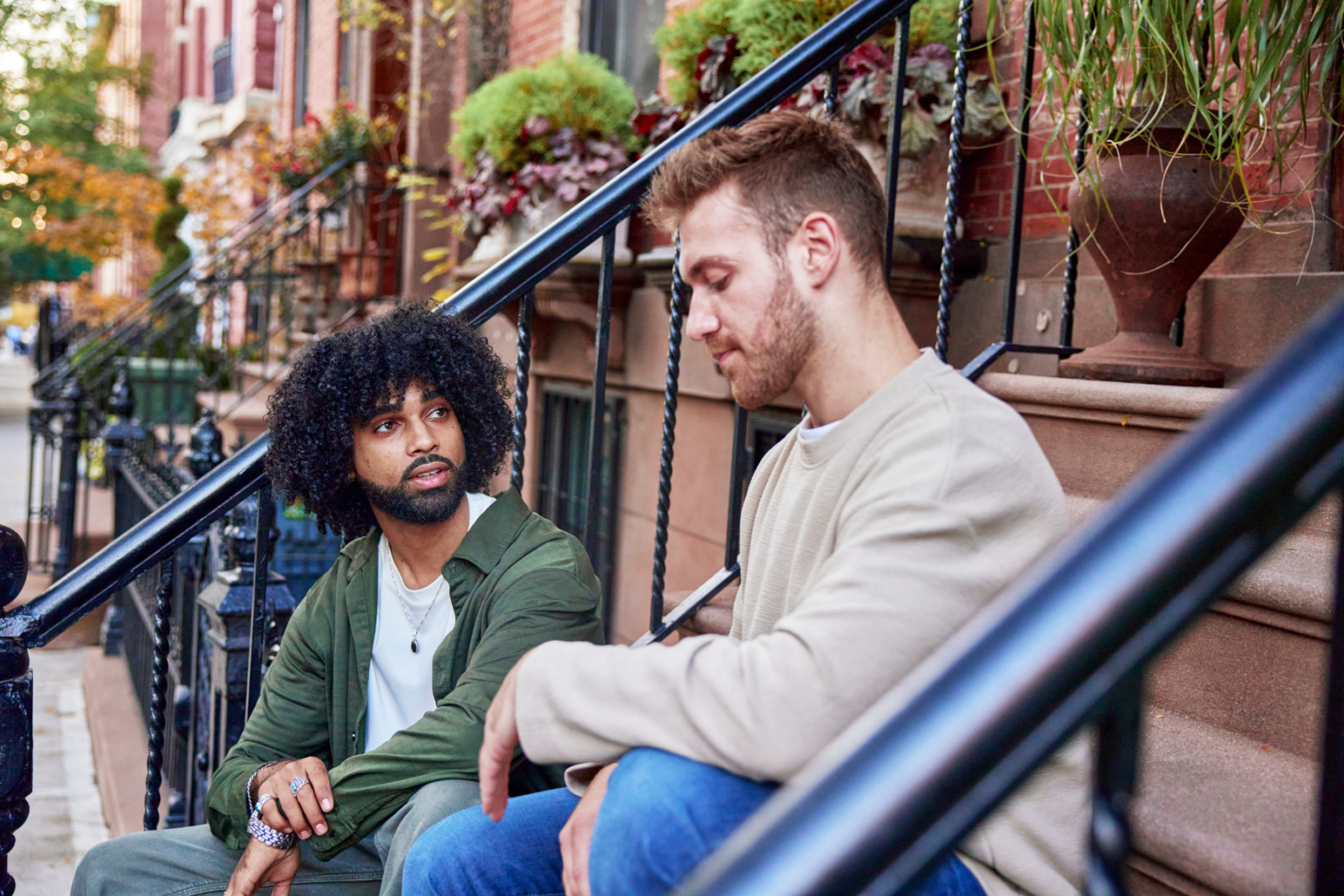 Male friends sitting down chatting in front of apartment