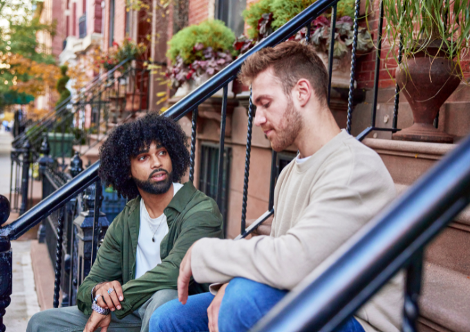 Male friends sitting down chatting in front of apartment