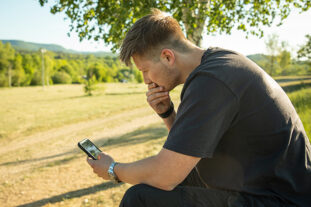 Man sitting alone outside thinking and looking at phone