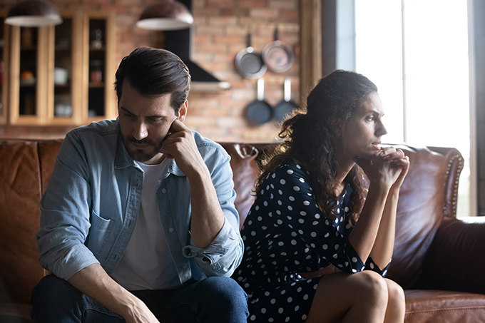 Couple sitting on couch looking away from each other serious