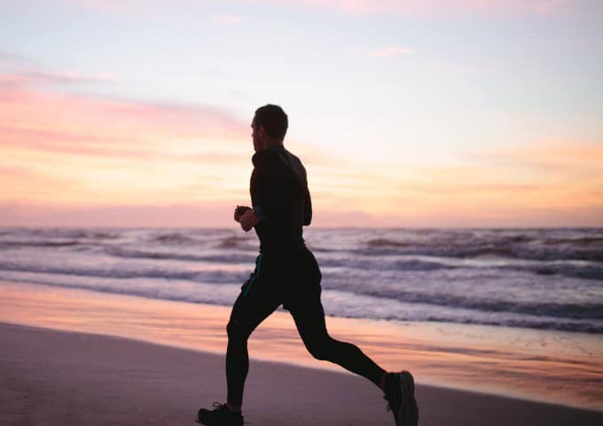 Silhouette of man running along the beach at sunrise