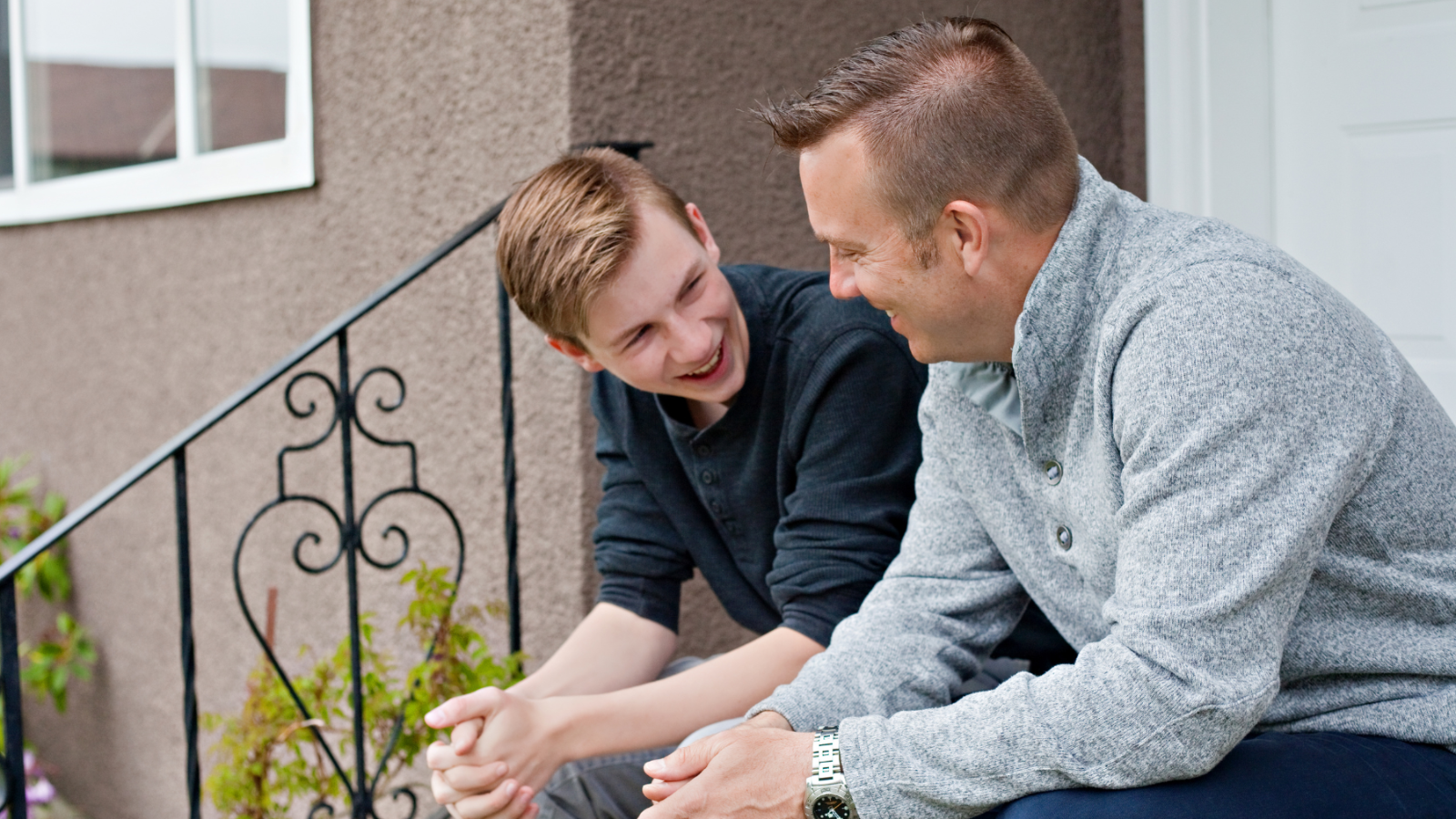Father and son sitting on a step outside smiling and chatting